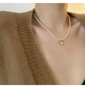 Detail of pink pearl necklace with golden heart pendant worn on a brown sweater