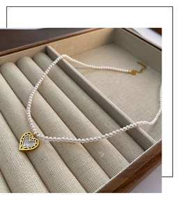 Detail of white pearl necklace with golden heart pendant in a soft jewelry box