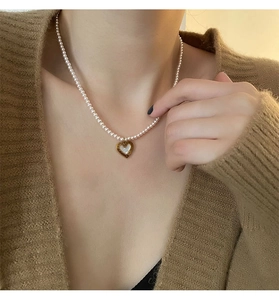 Close-up of heart pendant necklace with white pearls on a model wearing brown knitwear