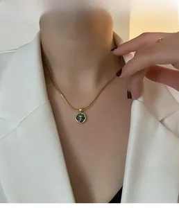 Close-up of a gold snake chain necklace featuring a green pendant with a rose relief