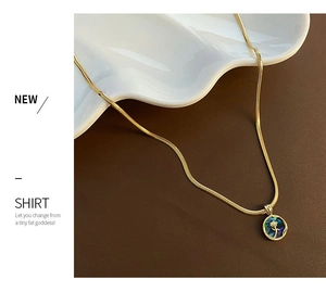 Detail of gold snake chain with embossed floral abalone shell pendant on white ceramic