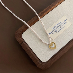 Pink pearl necklace with gold heart pendant displayed in a luxury wooden gift box