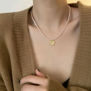 Pink pearl heart pendant necklace in gold-plated titanium steel worn on knit cardigan