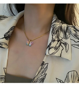 Gros plan d'un collier chaîne serpent dorée avec pendentif papillon iridescent sur modèle
