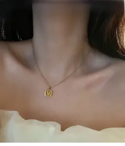 Close-up of a gold-plated square pendant necklace with a V-letter engraving on a model