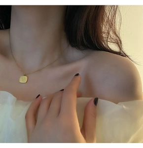 Close-up of minimalist gold square pendant necklace with V letter engraving on a model