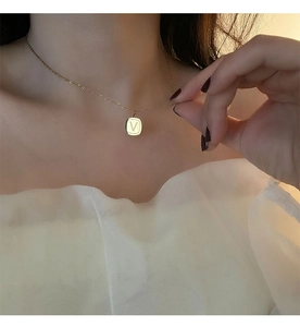 Close-up of gold titanium necklace featuring a square pendant with letter V engraving