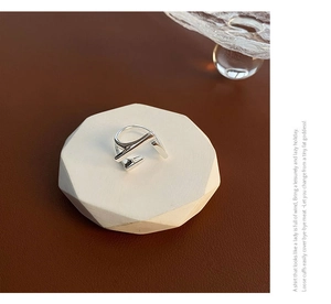 Close-up of geometric silver ring with minimalist layered lines on white stone tray