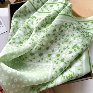 Macro shot of light green silk scarf with daisy and heart patterns in a gift box