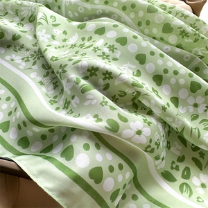 Macro detail of light green silk scarf with white floral and dark green heart patterns