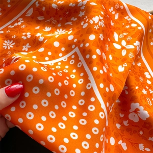 Detail shot of orange silk scarf featuring heart polka dots and floral patterns with glossy texture