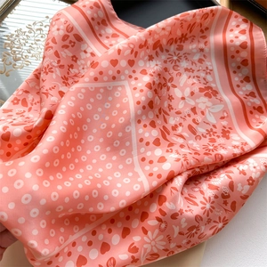 Close-up of coral pink silk scarf featuring white heart and floral patterns