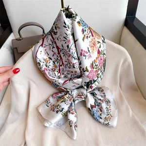Elegant floral print satin scarf with colorful botanical patterns on a soft beige knitwear