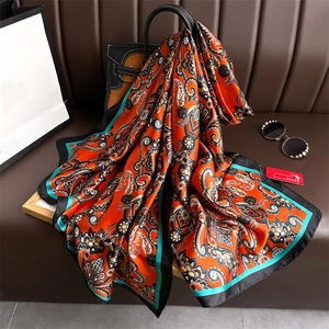 Détail d'un foulard en soie à motif paisley orange avec bordure verte sur canapé cuir