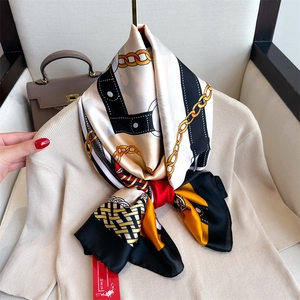 Detail of silk satin scarf with chain patterns tied elegantly on a beige knit sweater