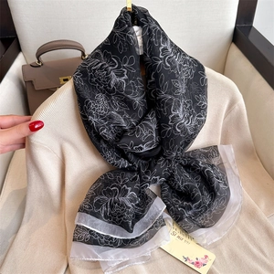 Détail d'un foulard en soie à fleurs noué sur tricot beige avec sac à main chic