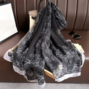 Détail d'un foulard en soie léger aux motifs floraux noir et blanc drapé sur un sac de luxe