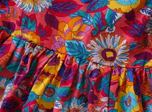 Detailed close-up of vibrant sunflower and floral prints on red pleated cotton dress fabric