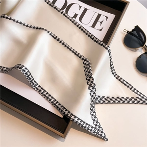 Elegant houndstooth silk scarf on ivory satin paired with stylish sunglasses and magazine