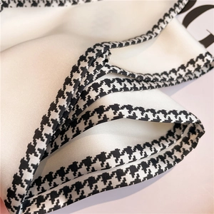 Close-up of luxury white silk scarf with classic black and white houndstooth border detailing