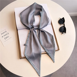 Grey houndstooth silk scarf with long narrow ribbon design displayed on a white book