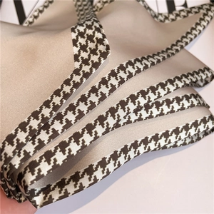 Close-up of houndstooth trim on a beige satin silk scarf with elegant fabric draping