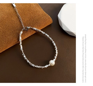 Détail d'un bracelet à perles argentées avec une perle ronde et un fermoir mousqueton