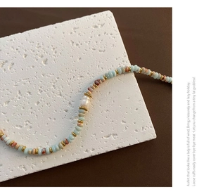 Détail d'un collier fait main avec des perles bleu clair et une perle baroque blanche