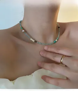 Detail einer Perlenkette mit grünen matten und goldenen Perlen am Hals des Models
