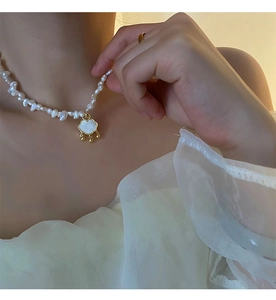 Detail of baroque pearl necklace with gold-rimmed shell lock pendant on a model