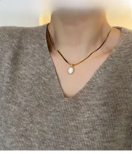 Close-up of golden flat snake chain necklace with oval white shell teardrop pendant