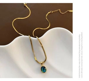 Detail of a gold snake chain necklace with an oval abalone shell teardrop pendant on ceramic