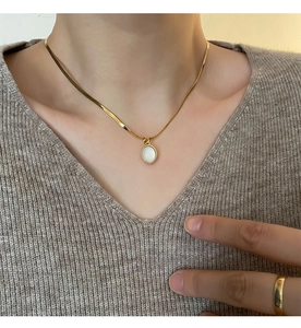 Detailed view of teardrop abalone shell pendant on gold snake chain with a wide band ring