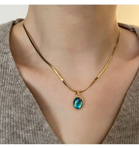 Detail of golden teardrop necklace with abalone shell inlay worn over a grey knit sweater