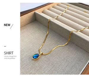 Close-up of golden snake chain with teardrop abalone shell pendant on beige velvet