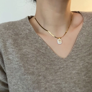 Close-up of golden snake chain necklace with white enamel zircon pendant on model