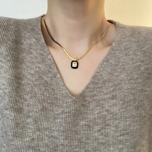 Close-up of golden snake chain necklace with black enamel pendant and clear zircon stone