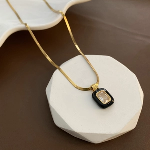 Detail of gold snake chain necklace featuring a black enamel pendant with zircon stone