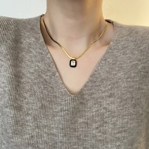 Elegant gold snake chain necklace with black square zircon pendant worn on a grey sweater