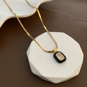 Gold snake chain necklace with black enamel pendant and rectangular zircon on a white stand