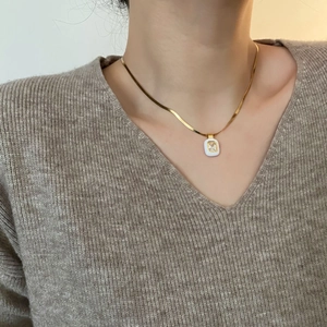 Gold snake chain necklace with square zircon pendant worn on a beige knit sweater