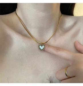 Gros plan d'un collier chaîne serpent dorée avec pendentif cœur et incrustation nacre
