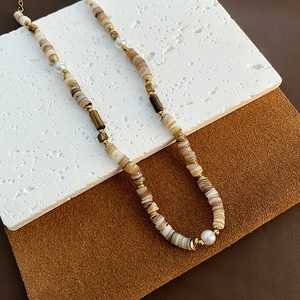 Collier artisanal perles de coquillage naturel et perles dorées sur fond texturé élégant