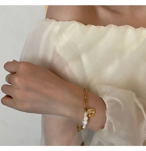 Detail of baroque pearl bracelet with gold chain and smiley charm on model wrist