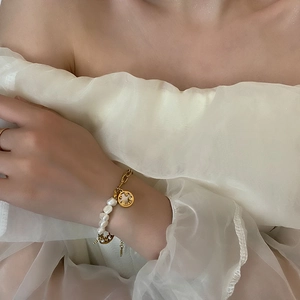 Baroque natural pearl bracelet with golden smiley face charm on a model's wrist