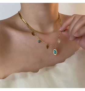 Dettaglio della collana a doppio strato dorata con ciondolo a foglia e pietra turchese