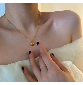 Golden titanium steel beaded necklace with sphere pendant on a female collarbone