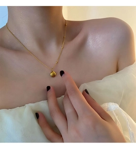 Detail of a minimalist gold bean pendant necklace worn by a model on the collarbone