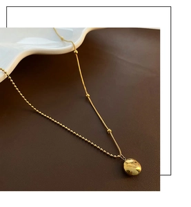 Detail of gold spliced chain necklace with a polished round pendant on a leather surface