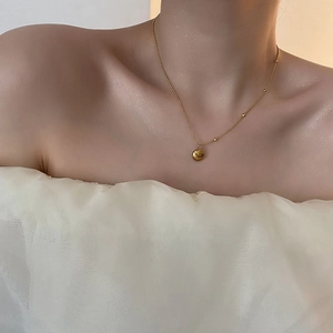 Minimalist gold ball pendant necklace in titanium steel on a woman's collarbone